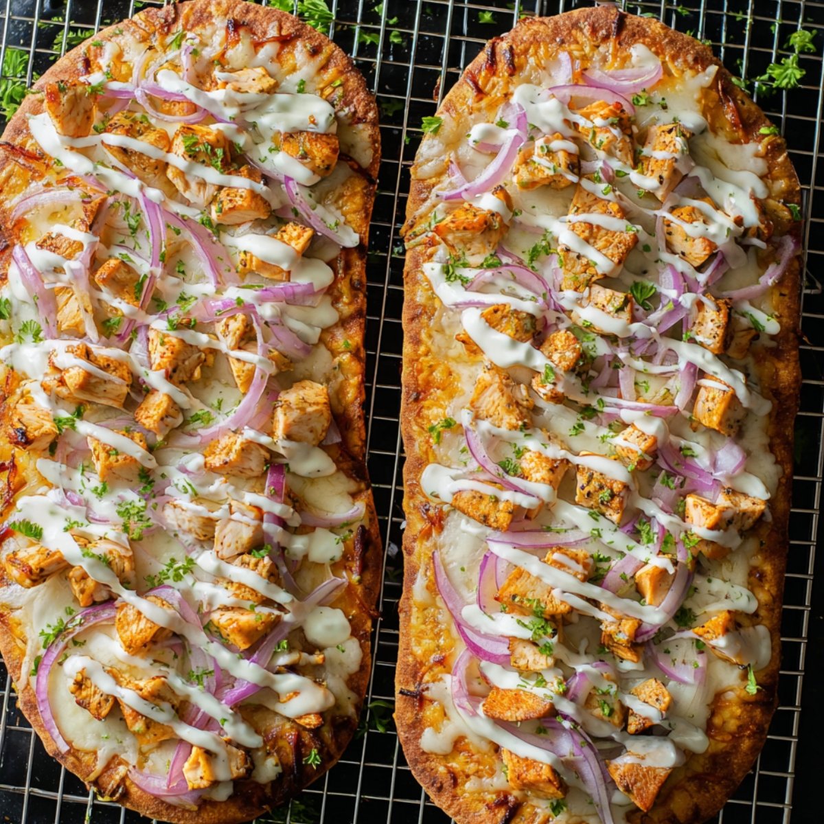 Two baked Buffalo Chicken French Bread Pizza topped with buffalo chicken, melted cheese, sliced red onions, and drizzled with ranch dressing, garnished with chopped parsley.