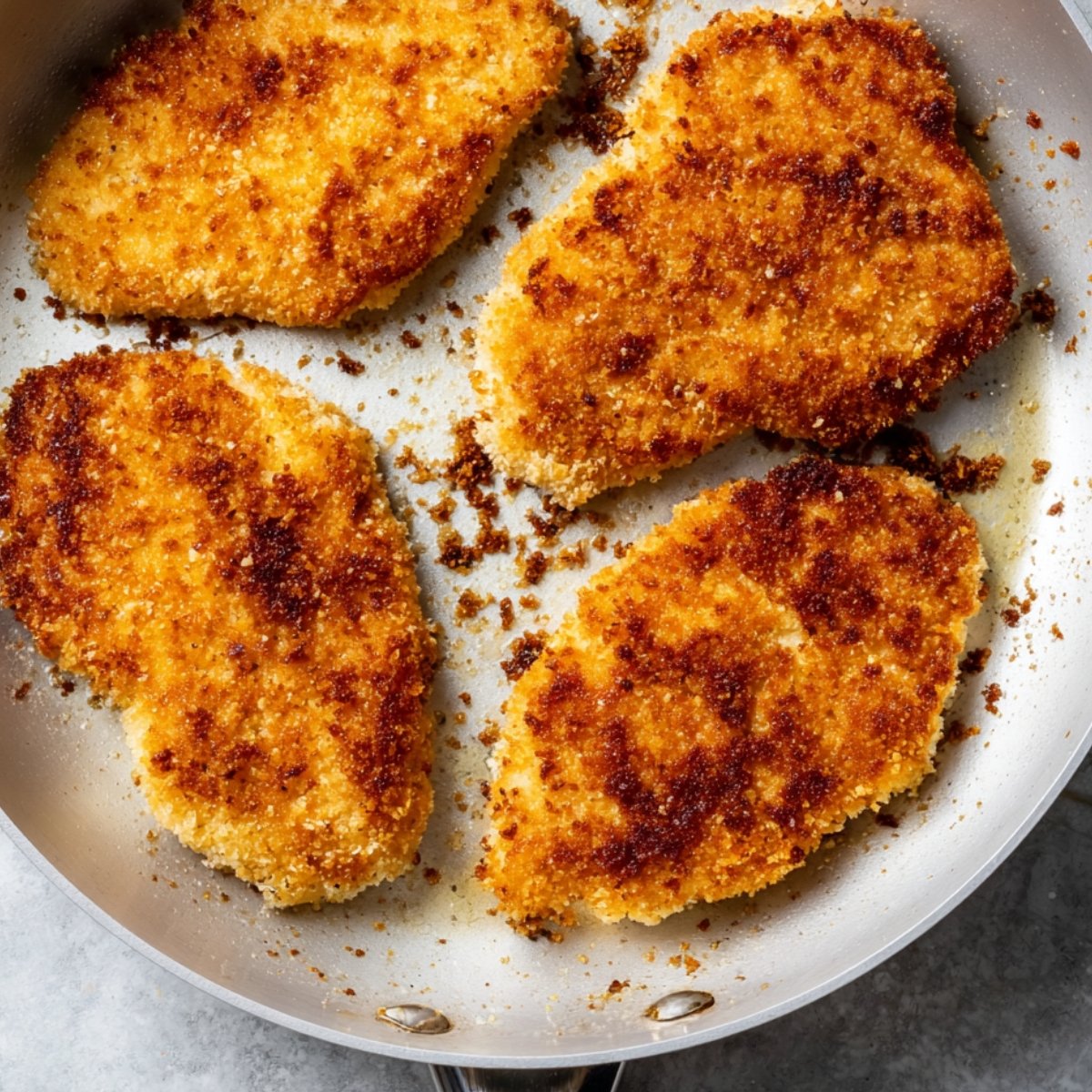 Golden-brown breaded chicken cutlets cooking in a skillet, crispy and evenly browned.