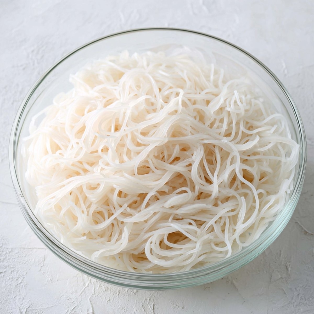 Bowl of plain cooked rice noodles, light and fluffy, ready for mixing with other ingredients.