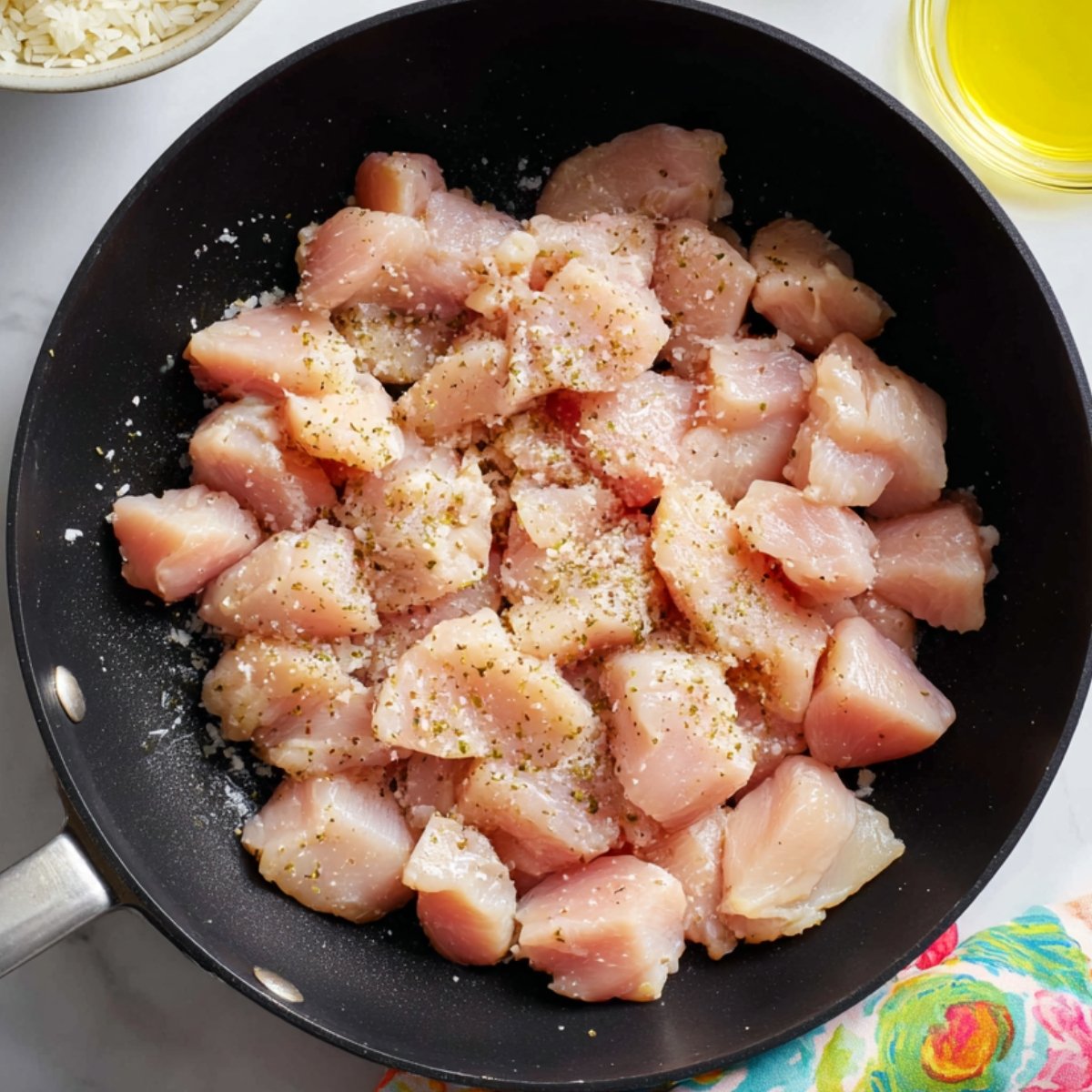 Raw diced chicken seasoned with salt and spices in a black skillet, ready to cook