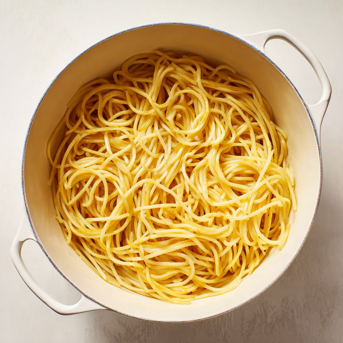 A top-down view of a large pot filled with cooked spaghetti noodles, lightly coated in oil, with the noodles slightly tangled.
