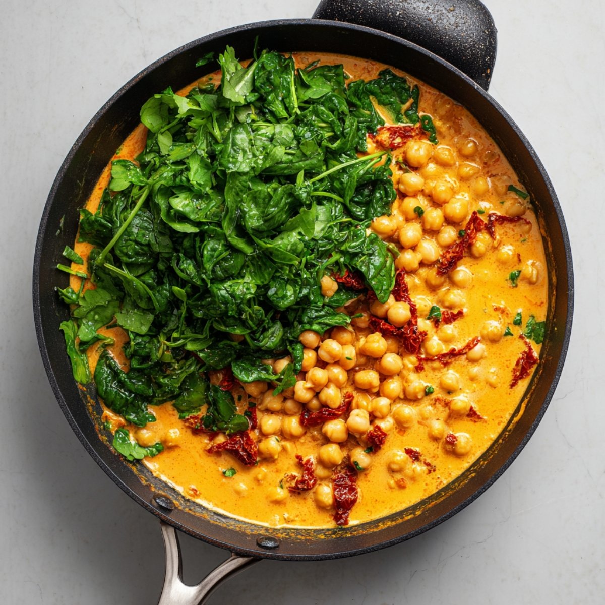 Chickpeas in a creamy orange curry sauce with fresh spinach added on top in a black skillet