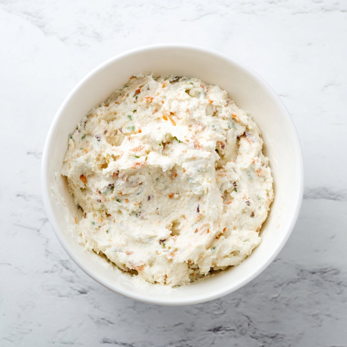 Bowl of creamy filling mixed with finely chopped vegetables and herbs, ready to use.