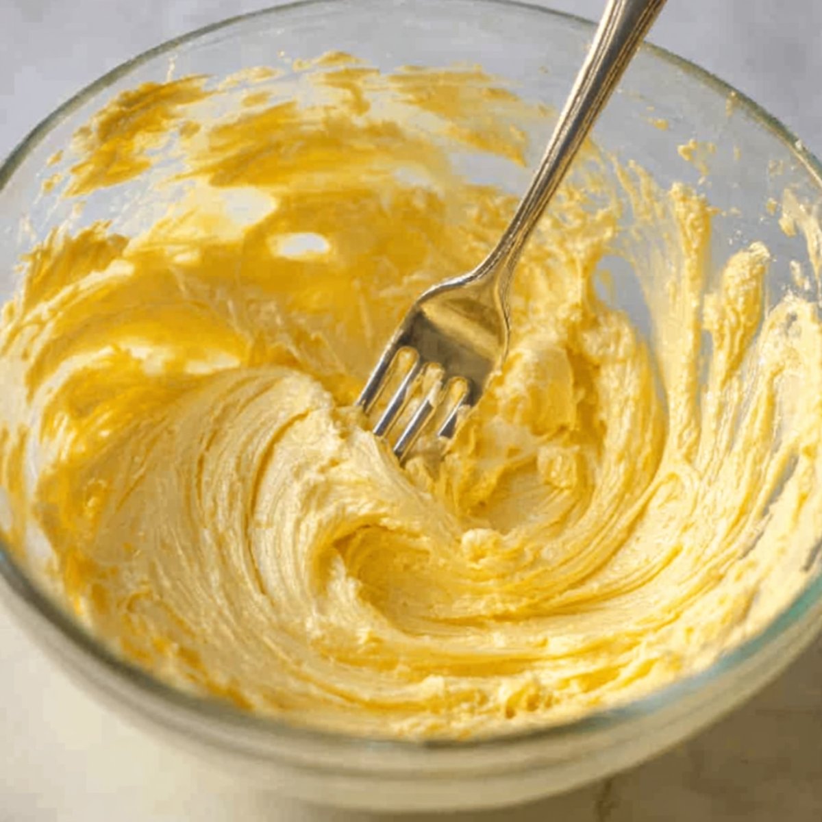 Overhead view of a glass bowl containing softened butter mixed with minced garlic, ready to be spread.