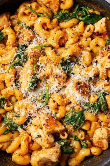 A skillet of creamy pasta with Marry Me Chicken Pasta and spinach, topped with grated cheese and freshly cracked black pepper, showing a hearty, golden pasta dish ready to serve.