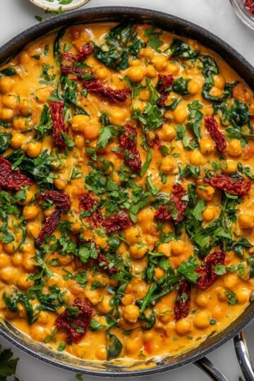 Creamy Marry Me Chickpeas curry with spinach and sun-dried tomatoes served in a skillet, garnished with fresh herbs