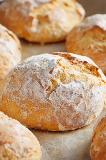 Freshly baked rustic Panini Bread rolls with a lightly floured, golden-brown crust, cooling on a baking sheet.