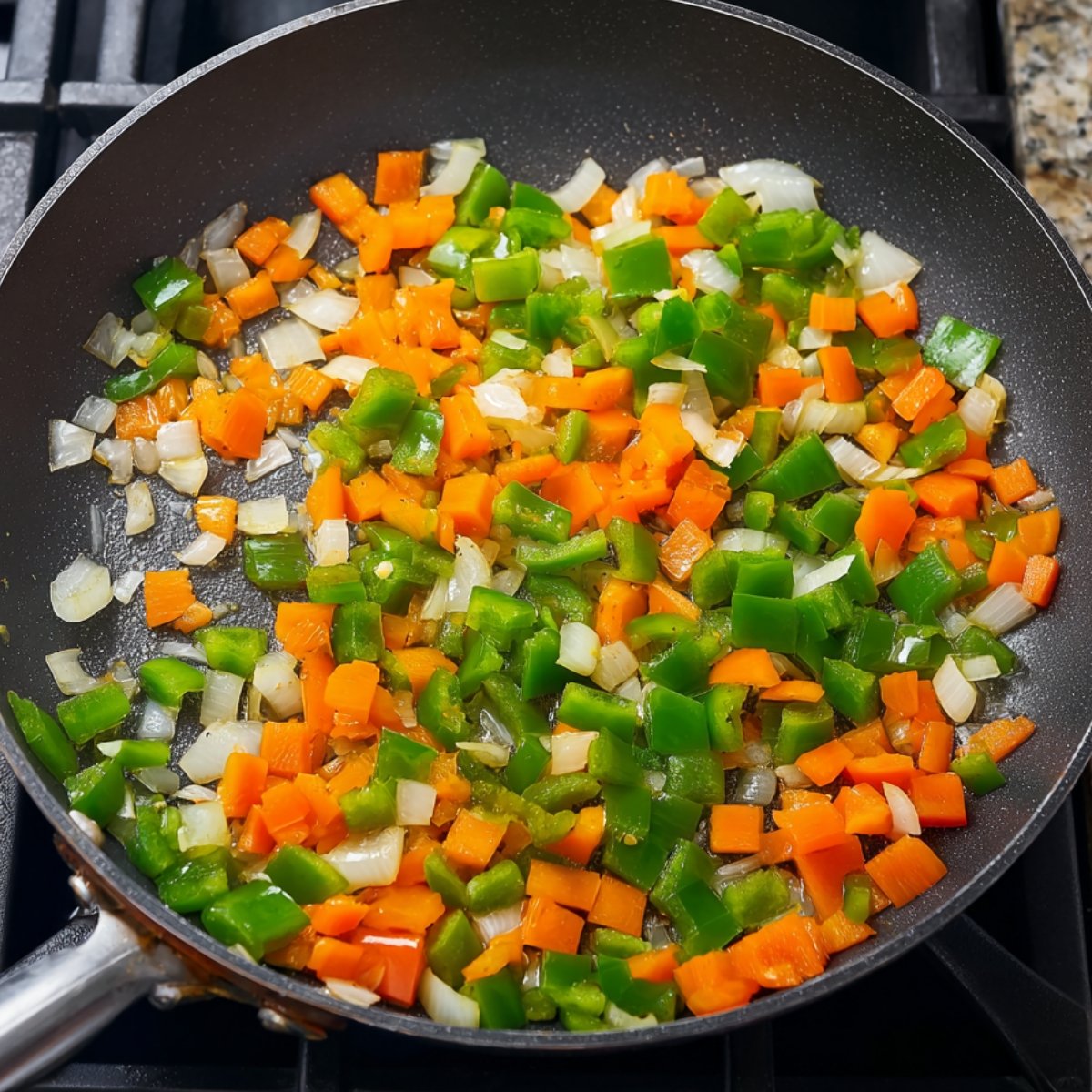 Sautéed diced green bell peppers, orange bell peppers, and onions cooking in a black skillet on a stovetop