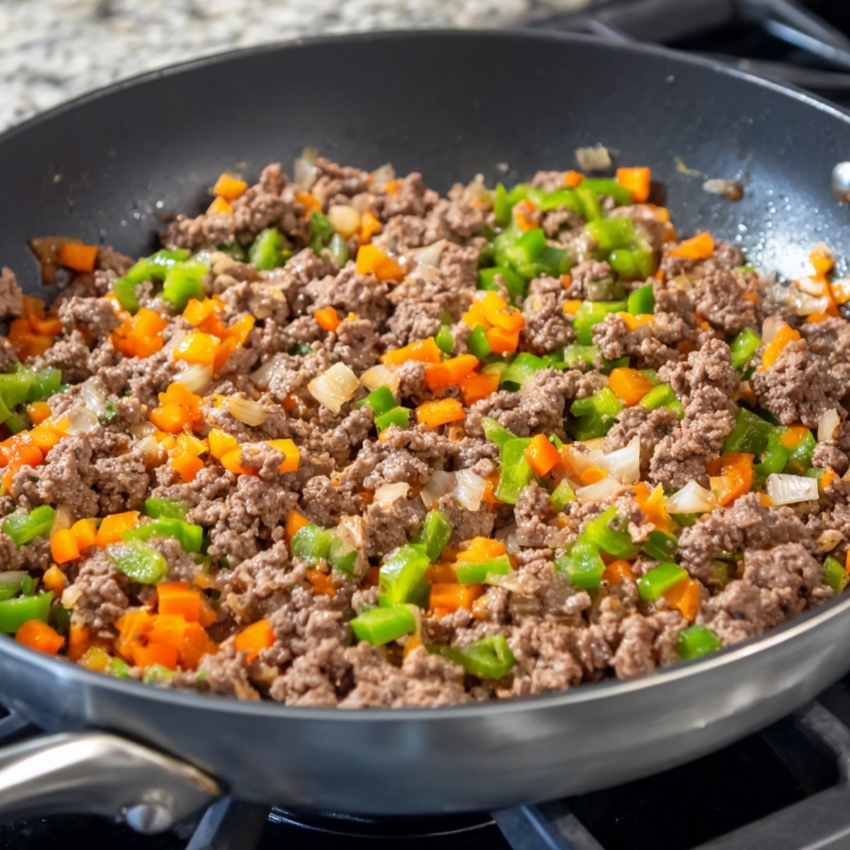 Ground beef cooked with diced green bell peppers, orange bell peppers, and onions in a black skillet on a stovetop