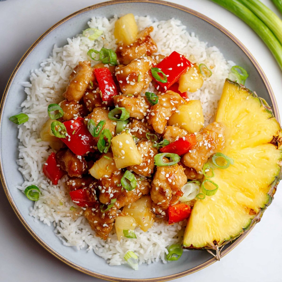 Pineapple Chicken and Rice stir-fry served over white rice on a plate, garnished with green onions and sesame seeds, with a pineapple slice on the side