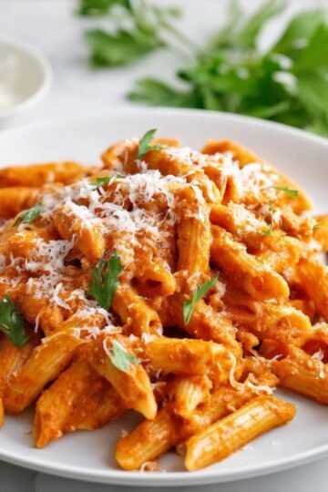 Creamy Pink Sauce Pasta coated penne pasta served on a white plate, garnished with grated cheese and fresh parsley, with a fork on the side