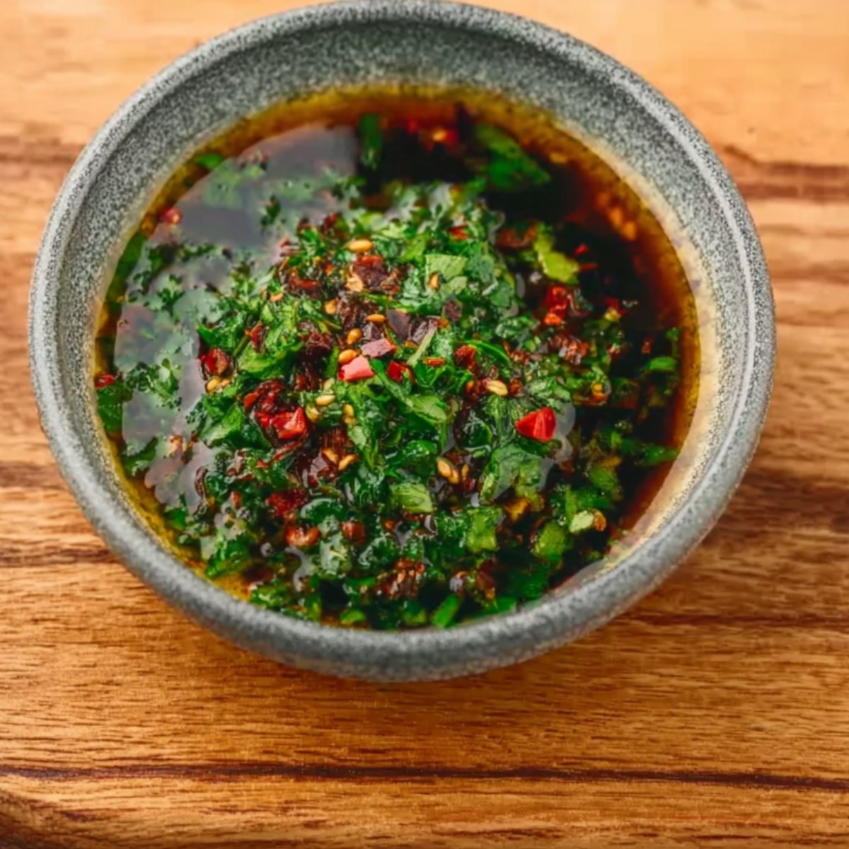A small gray bowl filled with a dark, herb-studded marinade, ready to be poured over mushrooms or other vegetables.