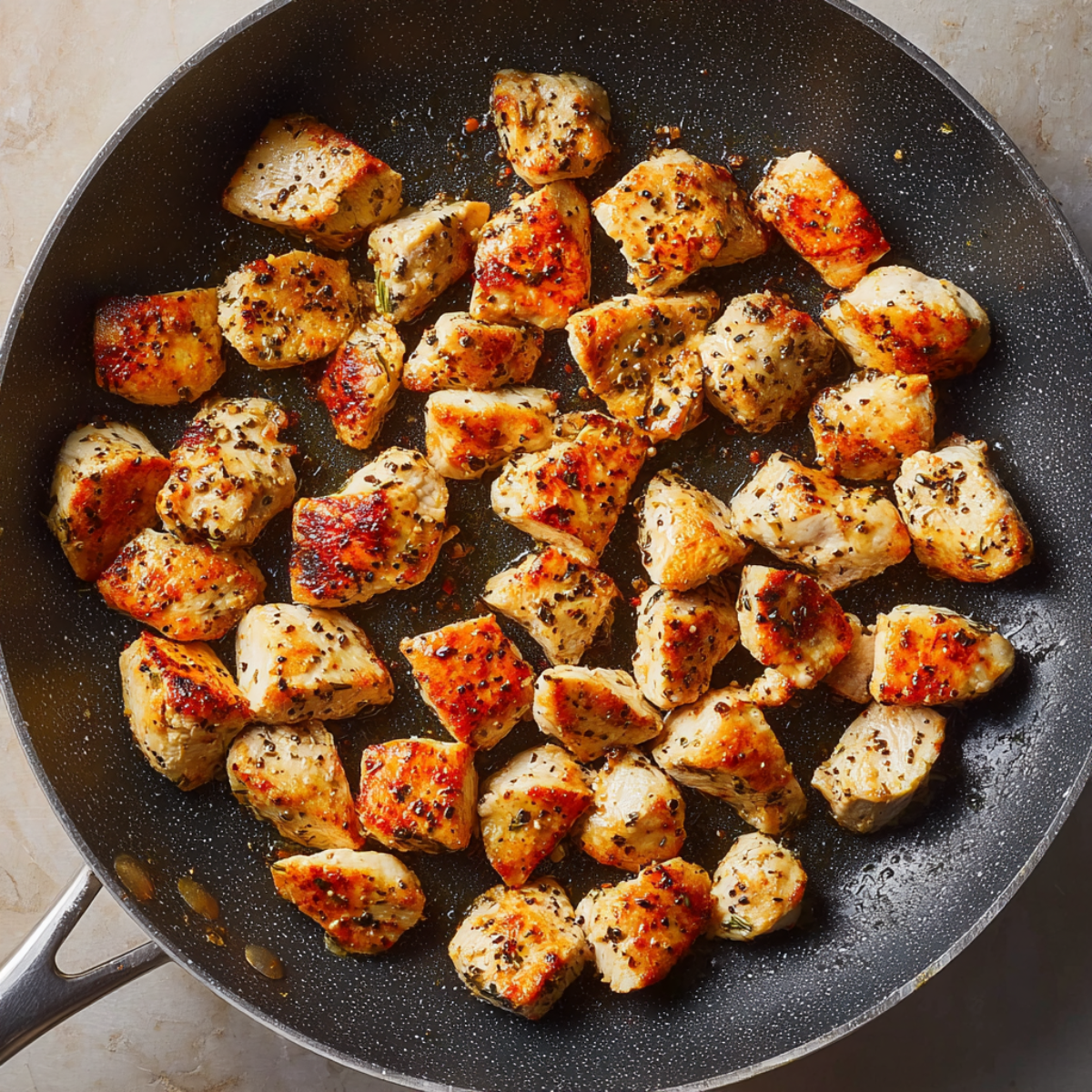 Bite-sized pieces of chicken breast being cooked in a black nonstick skillet, seasoned and browned on the outside.