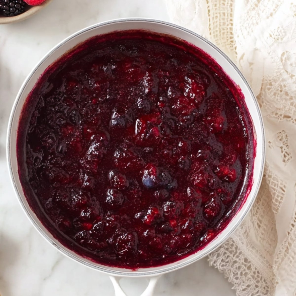 A top-down view of an unbaked pie crust on a marble countertop, surrounded by measuring cups and a small bowl of mixed berries including blueberries, raspberries, and blackberries.