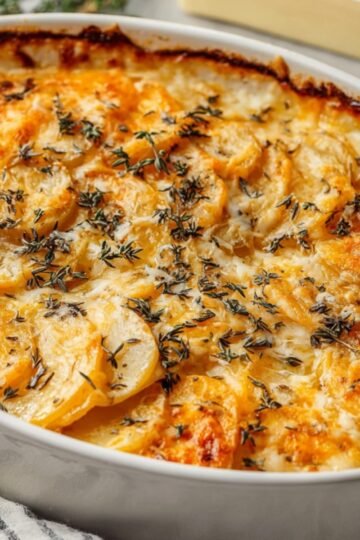 Baked root vegetable gratin in a white oval dish with a golden-brown cheesy crust, garnished with fresh thyme leaves