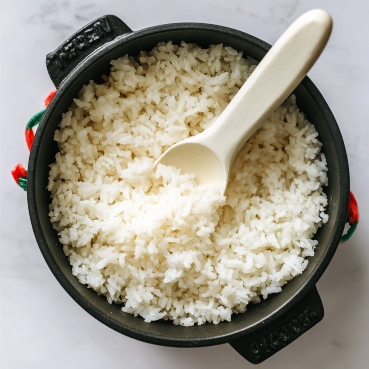 Cooked shredded chicken mixed with a creamy sauce and finely chopped green onions in a black bowl with a spoon