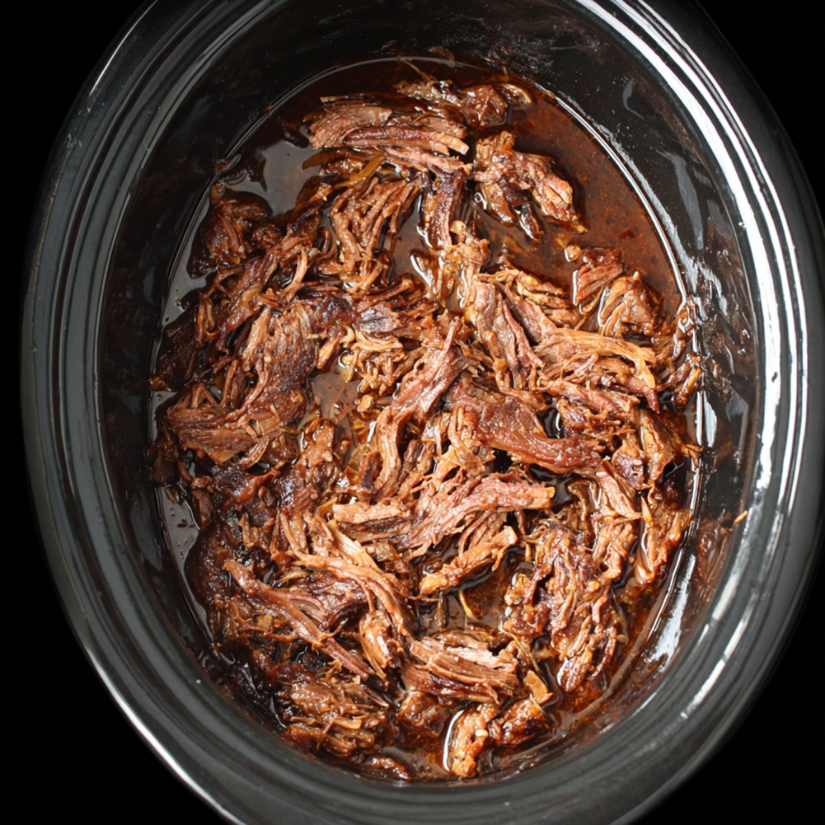 A top-down view of shredded slow-cooked beef in a slow cooker, coated in a thick, dark brown sauce.