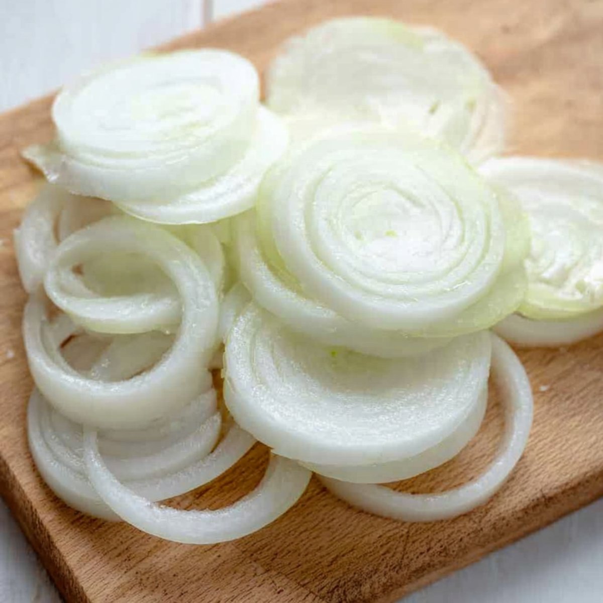 A pile of freshly sliced raw onion rings on a wooden cutting board, ready for cooking