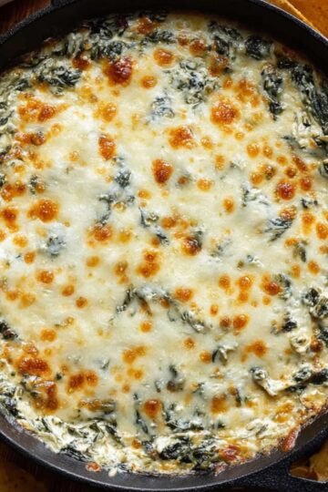 Baked spinach and artichoke dip in a cast iron skillet with melted golden-brown cheese on top surrounded by tortilla chips