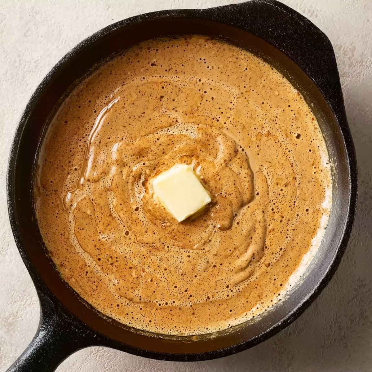 A cast-iron skillet with creamy garlic sauce, a pat of butter melting in the center, ready to be served over steak.
