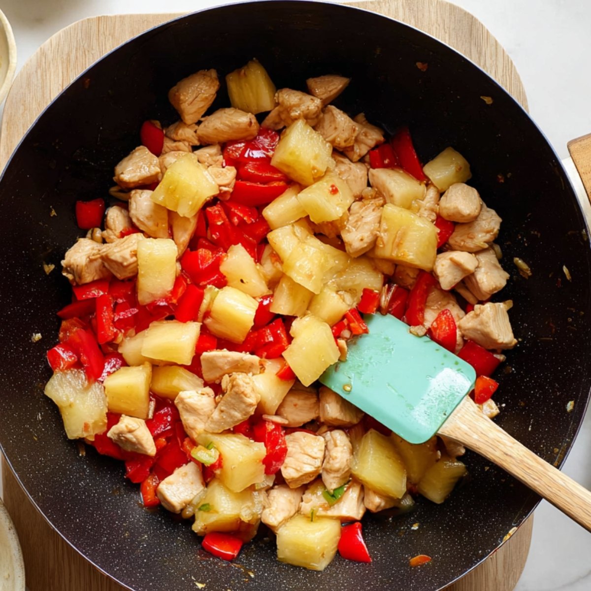 Pineapple chicken stir-fry served over white rice on a plate, garnished with green onions and sesame seeds, with a pineapple slice on the side