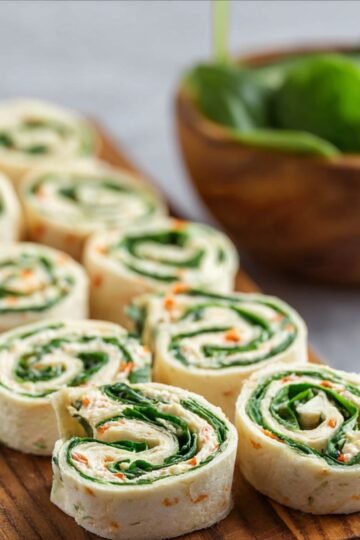 Sliced Turkey Pinwheels arranged on a wooden serving board, showing the spiral layers of tortilla, filling, and greens.