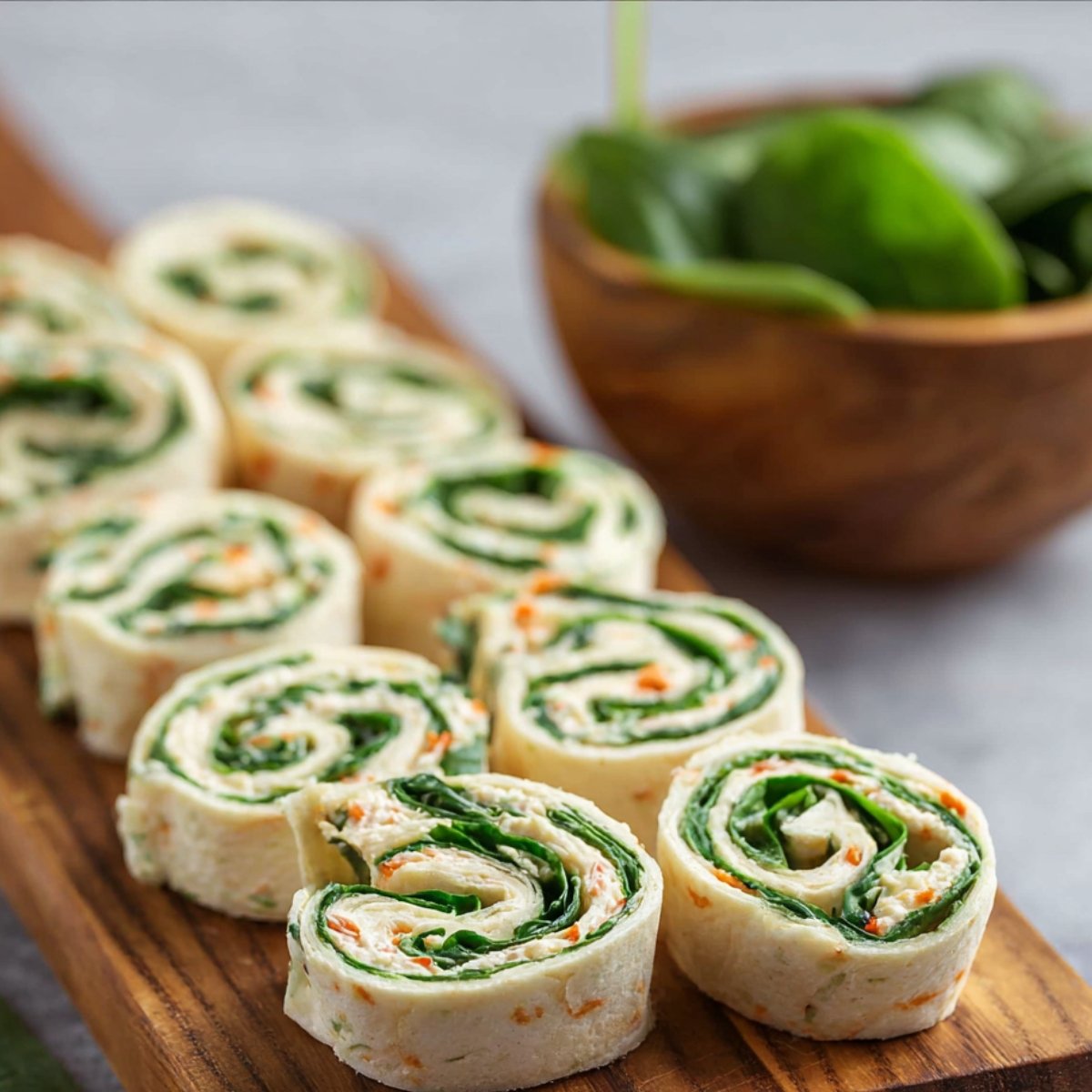 Sliced Turkey Pinwheels arranged on a wooden serving board, showing the spiral layers of tortilla, filling, and greens.
