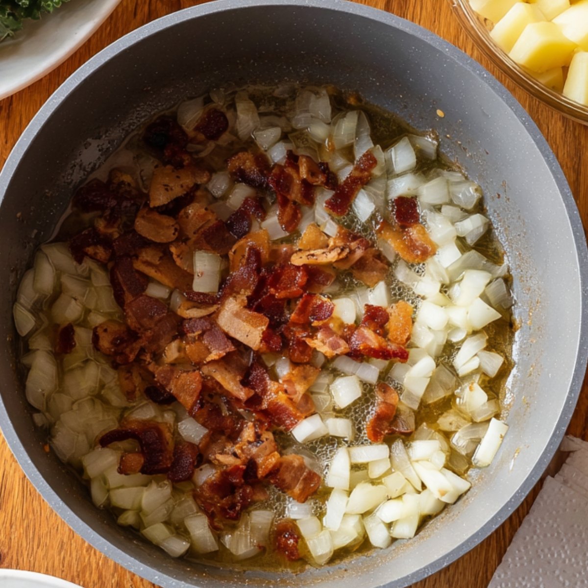 A skillet with diced onions and crispy bacon pieces sizzling in oil, ready to be added to soup.
